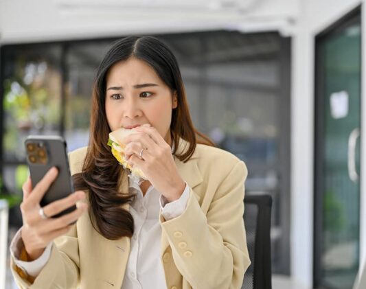 Asian women eating while using her phone