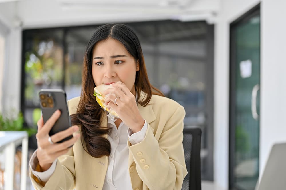 Asian women eating while using her phone